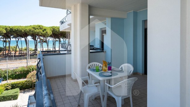 A balcony with a table and chairs, overlooking a beach with trees and a clear sky. - Second floor apartment with sea view (Pineto)