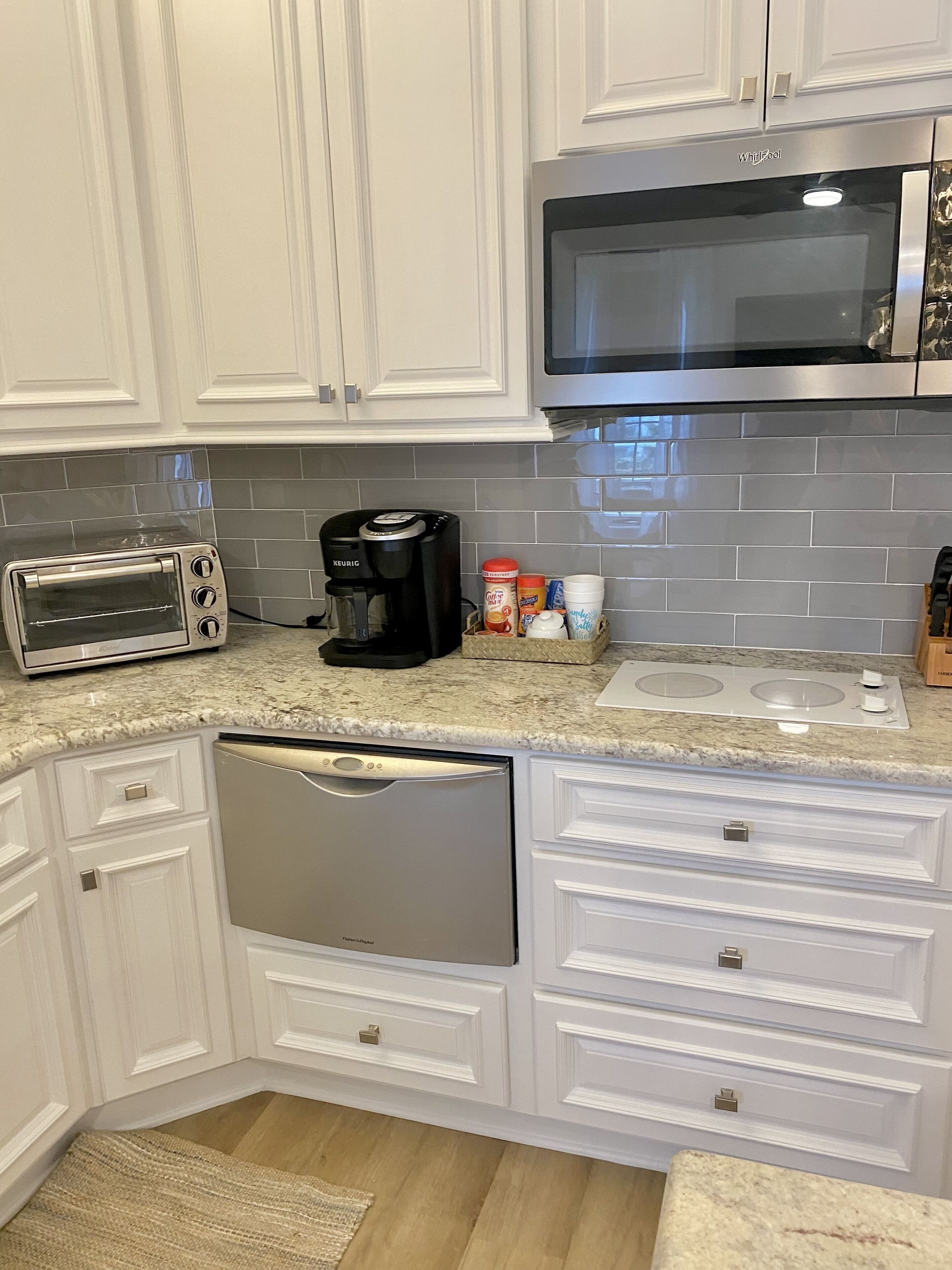 Una cucina con mobili bianchi, un forno a microonde, un tostapane, una macchina per il caffè e una lavastoviglie.