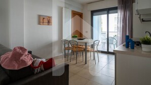 A modern living room with a sofa, a dining table with chairs, a kitchen area, and a sliding glass door leading to an outdoor balcony. - Holiday Rendez Vous 25 - First floor apartment with side sea view (Pineto)