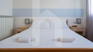 A neatly made bed with white linens and two rolled towels, a bedside table with a book, and a nightstand with a lamp. - Holiday Rendez Vous 25 - First floor apartment with side sea view (Pineto)