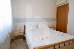 Een schone, goed verlichte slaapkamer met een enkel bed, nachtkastjes, een nachtkastje en een houten garderobe.