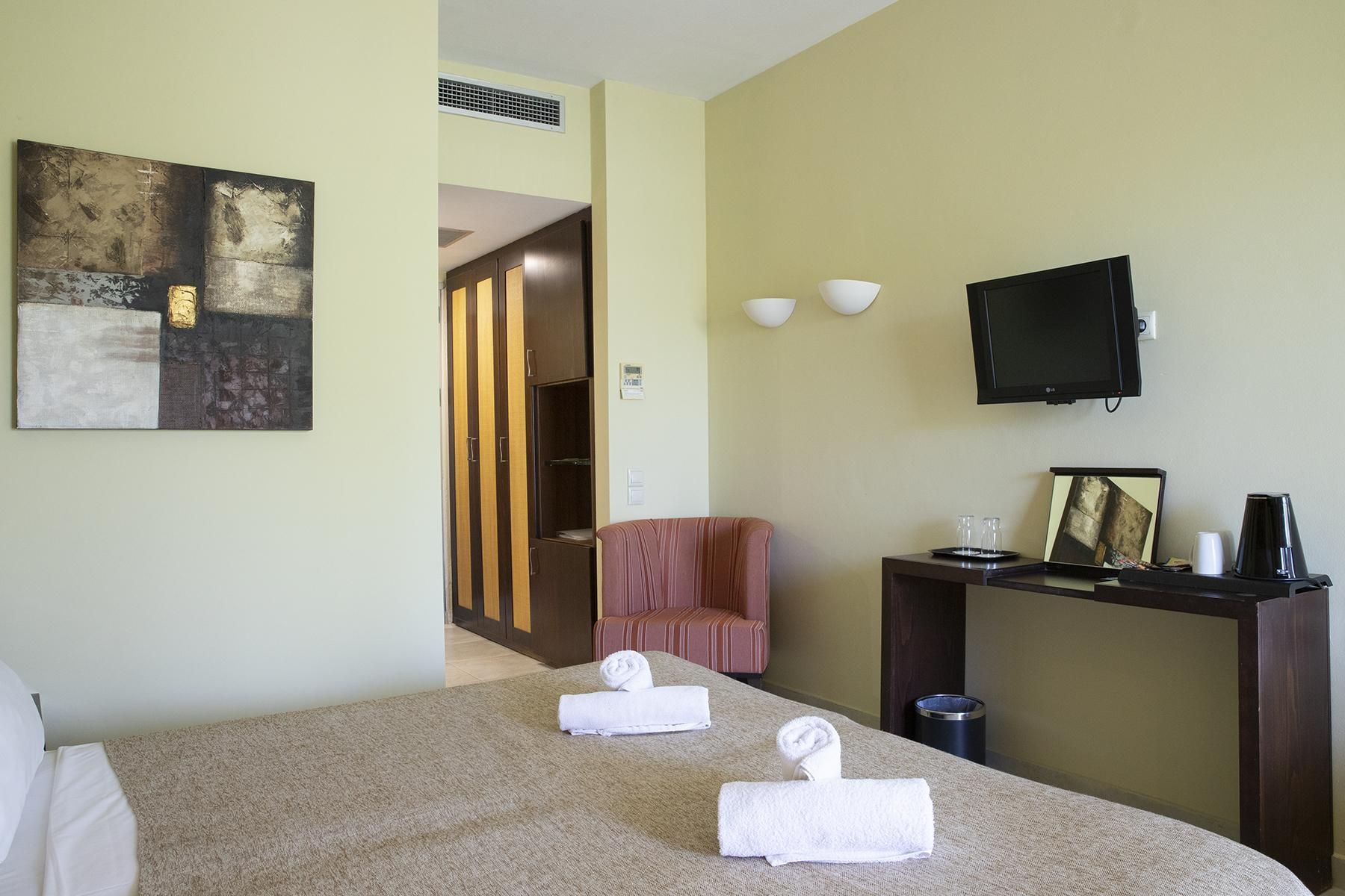 A hotel room with a bed, a desk with a television, a chair, and a painting on the wall.