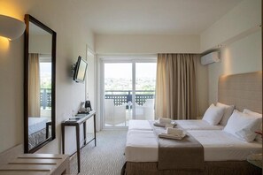 A hotel room with a large bed, a desk with a chair, a TV, and a balcony with a view.