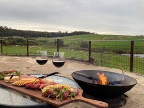 An outdoor dining setup with a charcuterie board, two glasses of red wine, and a fire pit. - MacManor - Cosy 2-Bedroom self contained BnB (Ferguson)