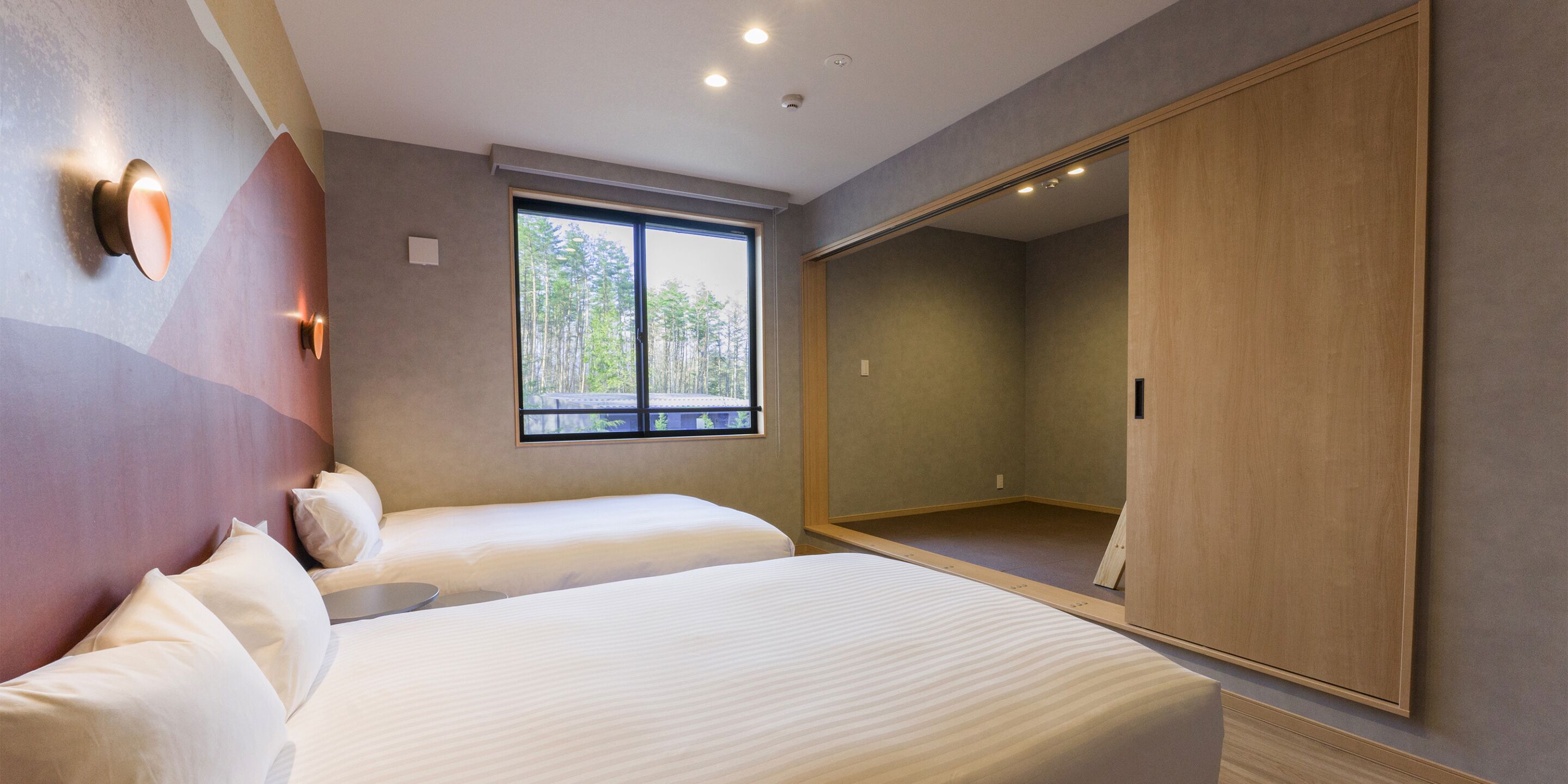 A modern hotel room with a large bed, a wardrobe, and a window with a view of trees.