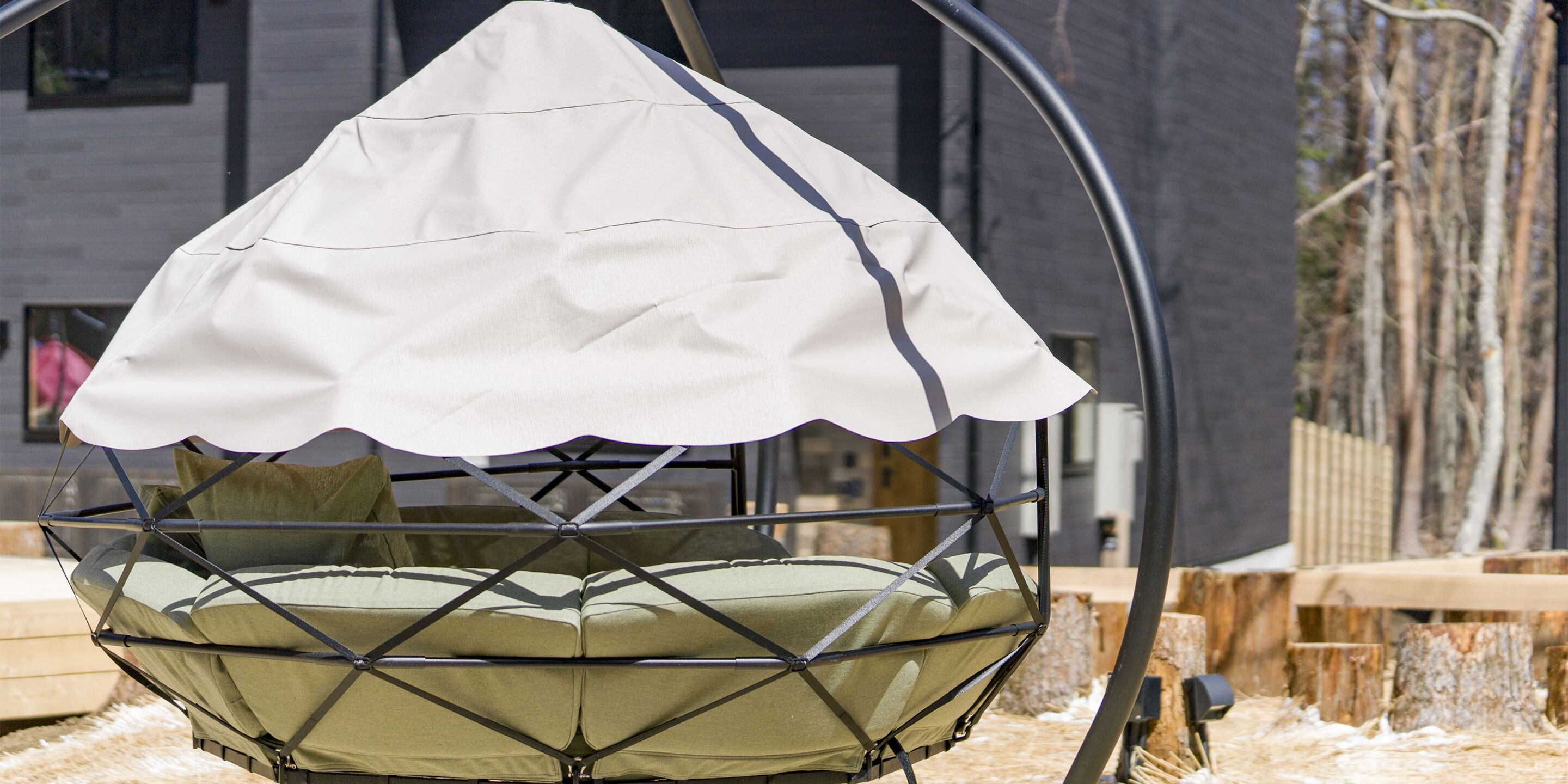 A hanging chair with a white canopy, green cushions, and a metal frame.