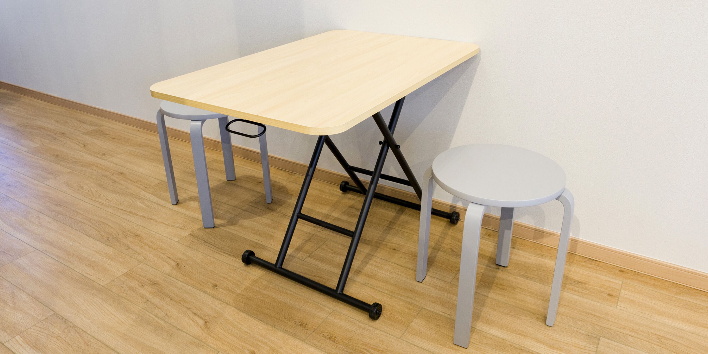 A small, light-colored wooden table with a metal frame and two metal legs, accompanied by a small white stool.