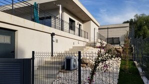 Un edificio moderno con balcón, un camino de piedra y un jardín vallado.