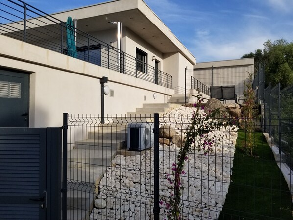 A modern building with a balcony, a stone pathway, and a fenced garden area. - Lecci de Porto Vecchio: Villa with a heated swimming pool, 6 minutes from Saint Cyprien Beach (Porto Vecchio)