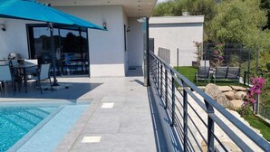 Un área de piscina moderna al aire libre con patio, zona de estar cubierta y vistas del paisaje circundante.