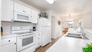 Eine moderne Küche mit weißen Schränken, einem Backofen, einer Mikrowelle und einem Kühlschrank. In der Mitte befindet sich eine große Kochinsel mit Spüle und einem Kronleuchter darüber.