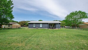 Ein eingeschossiges Haus mit einer Veranda, einem eingezäunten Garten und einem Baum im Hintergrund.