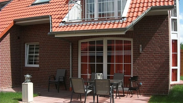 A house with a red-tiled roof, a balcony with a white railing, and a patio area with outdoor furniture.