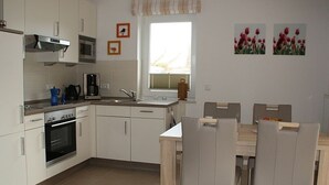 Una cucina moderna con mobili bianchi, un forno a microonde, una macchina per il caffè e un'area pranzo con tavolo e sedie.
