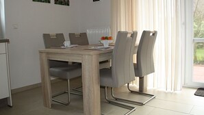 Un'area pranzo con un tavolo di legno, sedie grigie, un orologio appeso al muro e una finestra con tende.