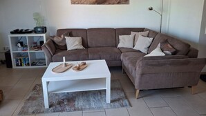 Un soggiorno con un divano marrone, un tavolino da caffè bianco, una libreria e un quadro raffigurante una spiaggia.