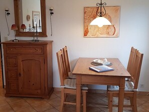 Ein Holztisch mit vier Stühlen, eine Kommode mit Schubladen, ein Wandspiegel und ein Gemälde über dem Tisch.