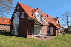 Et tosidet murhus med rødt tegltag, store vinduer og en terrasse med udendørs møbler.