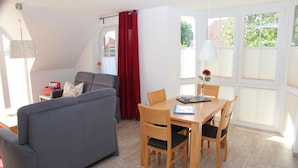 A modern living room with a grey sofa, a wooden dining table with chairs, and a window with blinds.