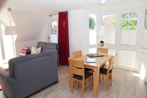 Ein modernes Wohnzimmer mit einem grauen Sofa, einem Holzespeisetisch mit Stühlen und einem Fenster mit Jalousien.
