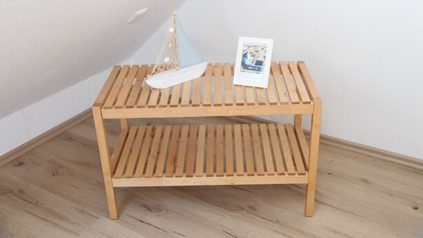 A wooden bench with a lower shelf, a small hanging net, and a framed picture.