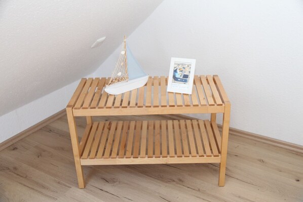 A wooden bench with a lower shelf, a small hanging net, and a framed picture.