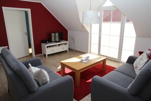 Ein modernes Wohnzimmer mit roter Akzentwand, einer weißen Unterhaltungseinheit und einem großen Fenster, das natürliches Licht hereinlässt.