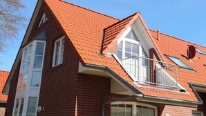 A two-story house with a red-tiled roof, a visible chimney, and a satellite dish.