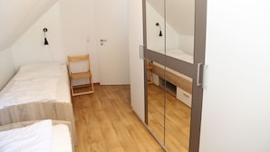 A small, well-lit room with a sloped ceiling, a wooden floor, a single bed, a wooden chair, and a wardrobe with a mirror.