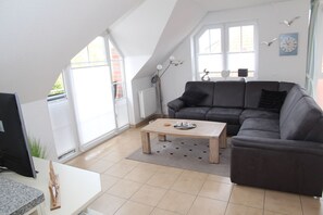 Ein modernes Wohnzimmer mit einem grauen Sofa, einem Holztisch und einem Fernseher auf einem weißen Schrank.