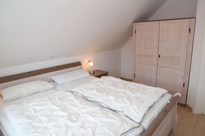 A bedroom with a bed, a bedside lamp, a wardrobe, and a sloped ceiling.