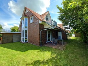 A two-story house with a brick exterior, a glass conservatory, and a patio with outdoor furniture. - Hummel Hummel - Dog-friendly vacation apartment (70sqm) for 4 people with garden (Krummhörn)