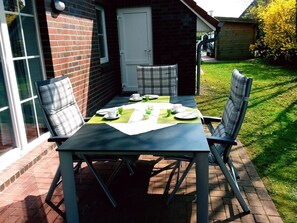 A patio table with chairs, a door, and a brick wall. - Hummel Hummel - Dog-friendly vacation apartment (70sqm) for 4 people with garden (Krummhörn)