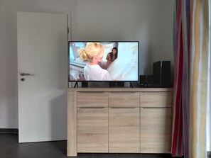 Un televisor sobre un mueble de madera con puerta y una cortina al fondo.