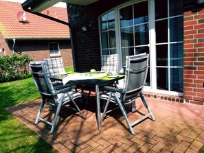 A patio with a table and chairs, a brick wall, and a window. - Hummel Hummel - Dog-friendly vacation apartment (70sqm) for 4 people with garden (Krummhörn)