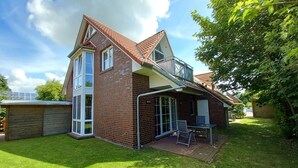 A two-story house with a brick exterior, a glass conservatory, and a patio with outdoor furniture.