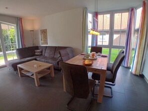 Una sala de estar con un sofá, una mesa de comedor con sillas, una mesa de centro y una ventana con cortinas.