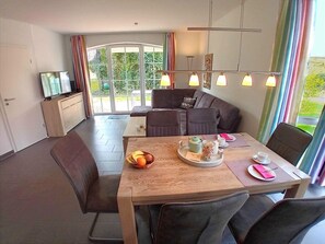 Un comedor moderno con una mesa de madera, sillas y un sofá. Hay un televisor sobre un mueble a la izquierda.