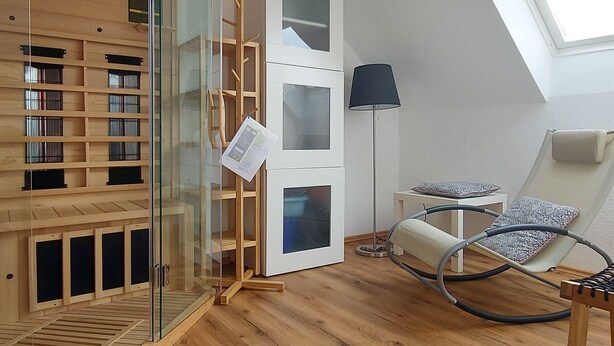 Un dormitorio tipo loft moderno con techo inclinado, estanterías de madera, cabina de ducha de vidrio, lámpara de pie y sillón de masajes.