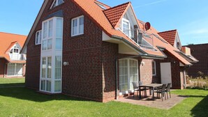 Una casa de ladrillo de dos pisos con techo inclinado, ventanas grandes y un patio con mobiliario exterior.