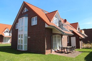Ein zweigeschossiges Backsteinhäuschen mit geneigtem Dach, großen Fenstern und einer Terrasse mit Gartenmöbeln.