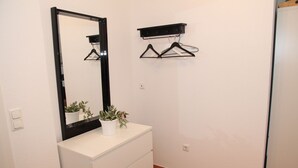 Une salle de bain avec un meuble-lavabo blanc, un miroir et une étagère sur laquelle sont accrochés deux cintres noirs.