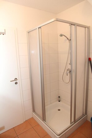 A corner shower with a glass door, white tiled walls, and a tiled floor.