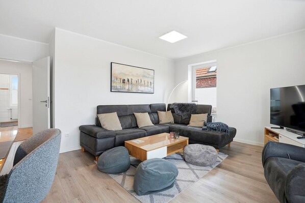 Un salon moderne avec un canapé d’angle, une table basse et un téléviseur.