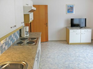 Cocina compacta con estufa, lavamanos y un pequeño armario con televisor.