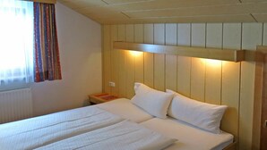 A double bed with a wooden headboard, a bedside table with a book, and a window with curtains. - Cosy apartment for 13 guests with WIFI, TV and balcony (See)