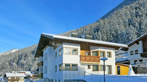 A multi-story hotel with a balcony, surrounded by snow-covered trees and mountains. - Cosy apartment for 13 guests with WIFI, TV and balcony (See)