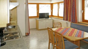 A compact kitchen with a stove, sink, and a small dining area with a table and chairs. - Cosy apartment for 13 guests with WIFI, TV and balcony (See)