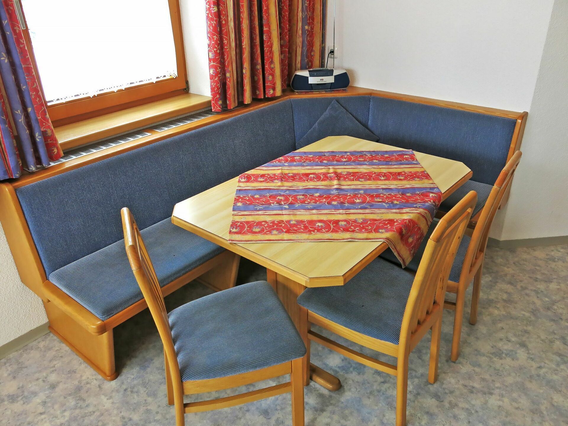 Un coin salon avec une table, des chaises rembourrées bleues et une nappe à motifs.
