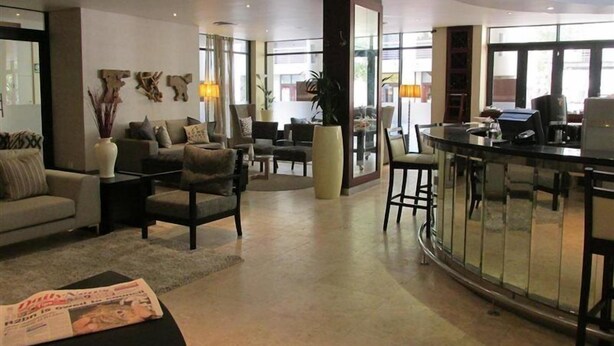 A hotel lobby with a seating area, a reception desk, and large windows.